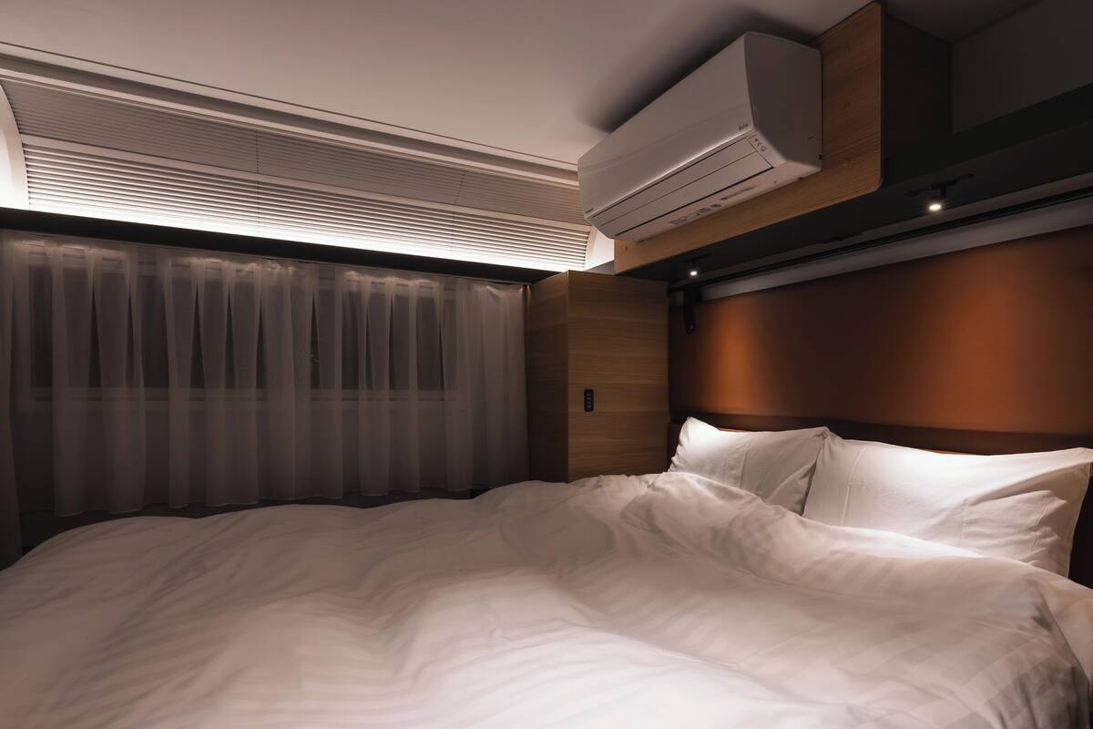 A modern hotel room with a large bed, a built-in air conditioning unit, and a wooden headboard.