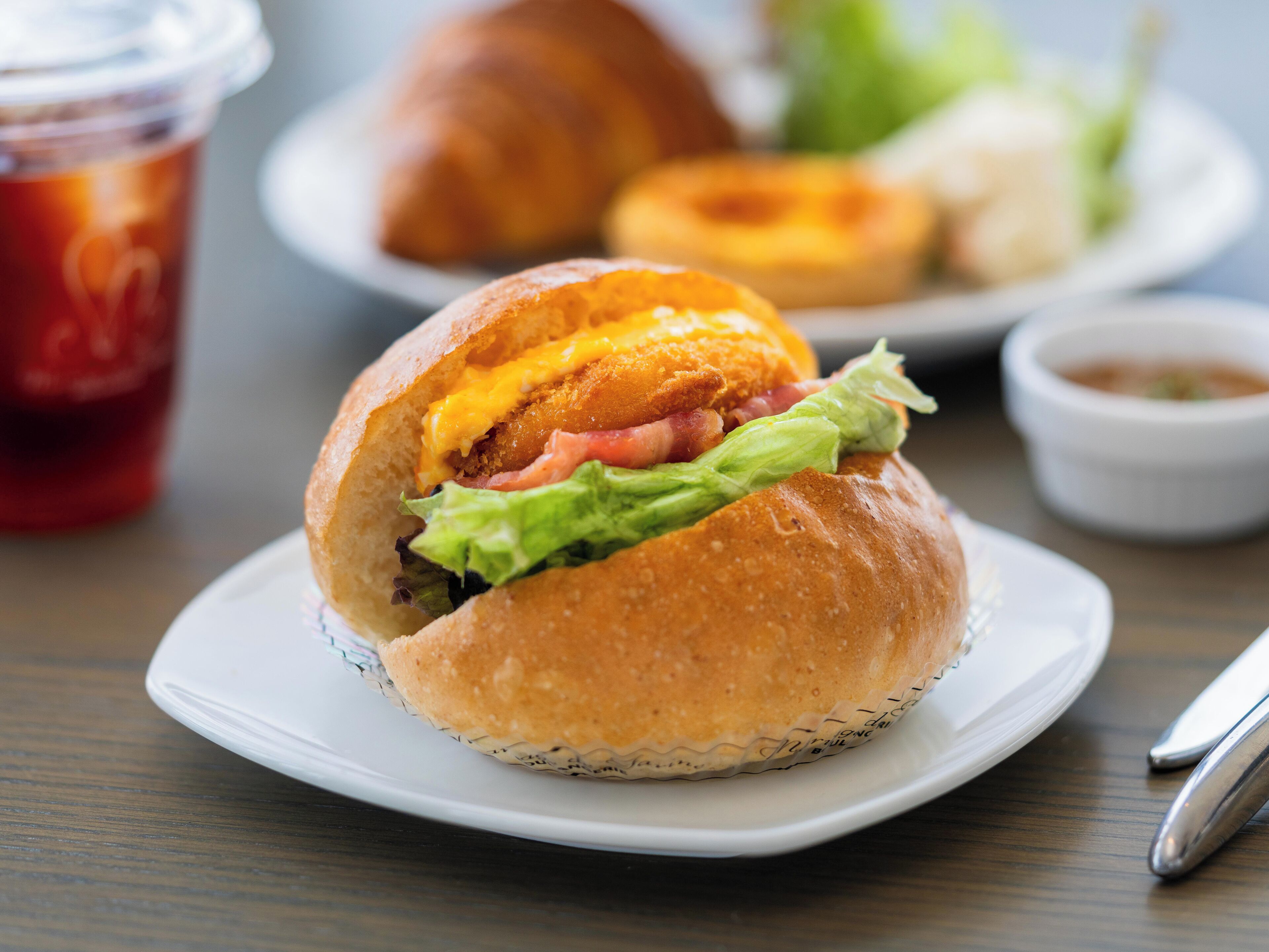 Un sándwich sobre un plato blanco, con una bebida al fondo.