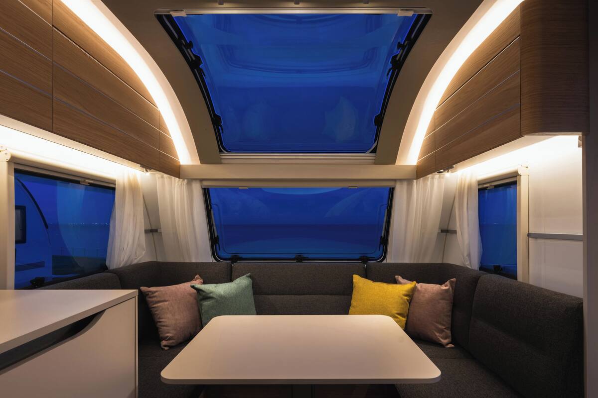 A modern train interior with a central seating area, a table, and two large windows offering a view of the night sky.