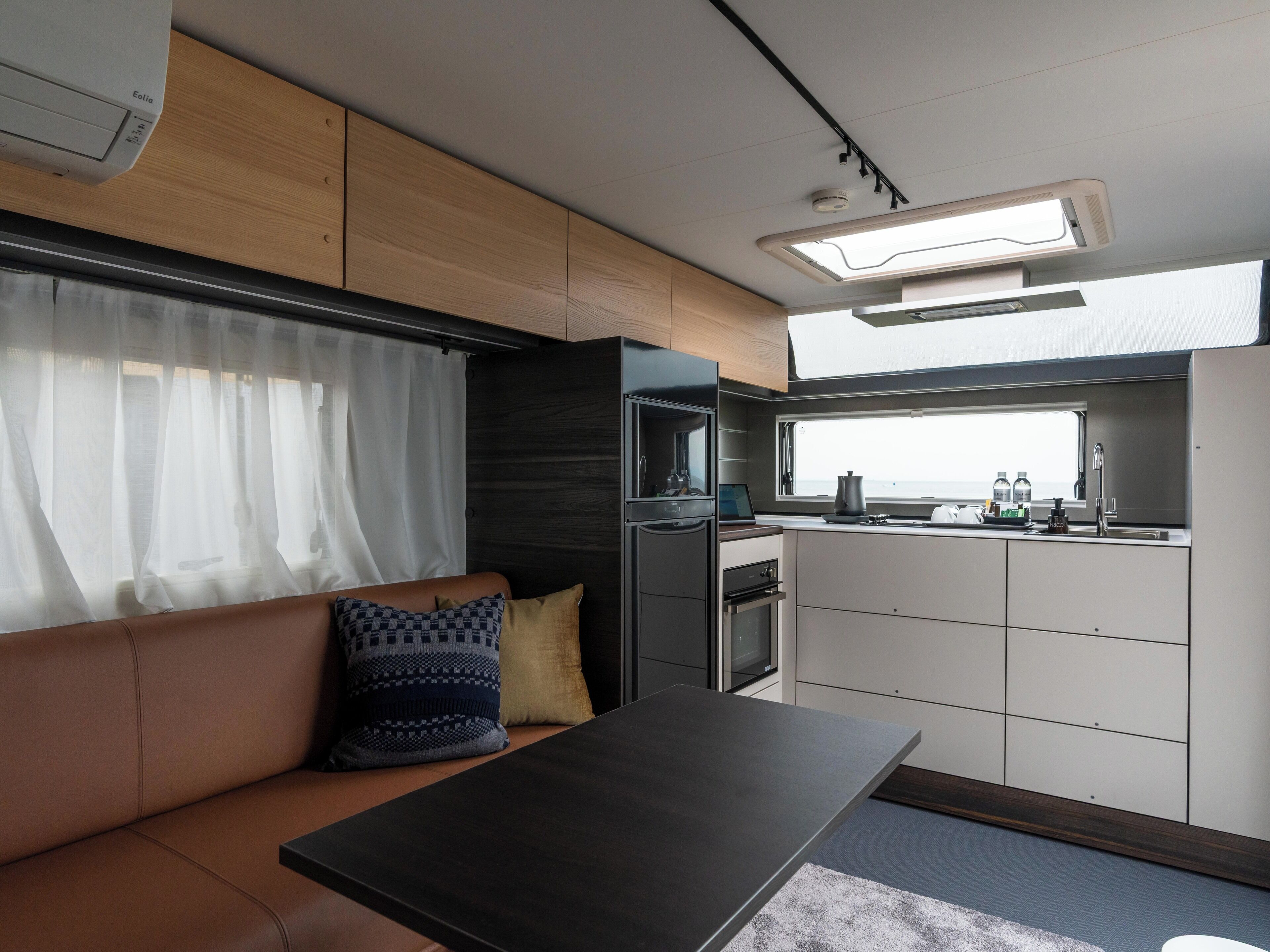 A compact kitchenette with a window, a sofa with cushions, and a table.