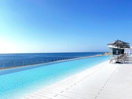 Una piscina azul cristalina con cubierta blanca, barandilla de vidrio y vista al océano.