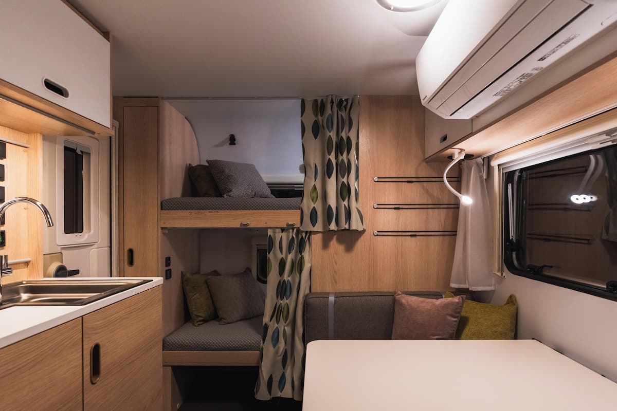 A compact RV interior with a kitchenette, a dining area, and a sleeping loft.