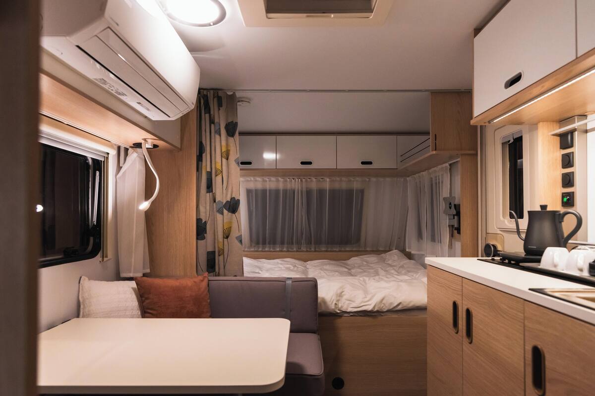 A compact RV interior with a kitchenette, a bed, and a seating area.