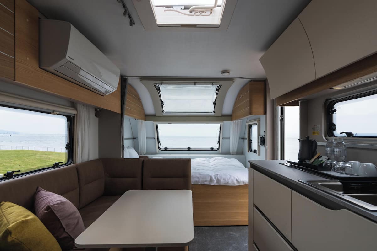 A compact RV interior with a kitchenette, a dining area, and a sleeping berth.