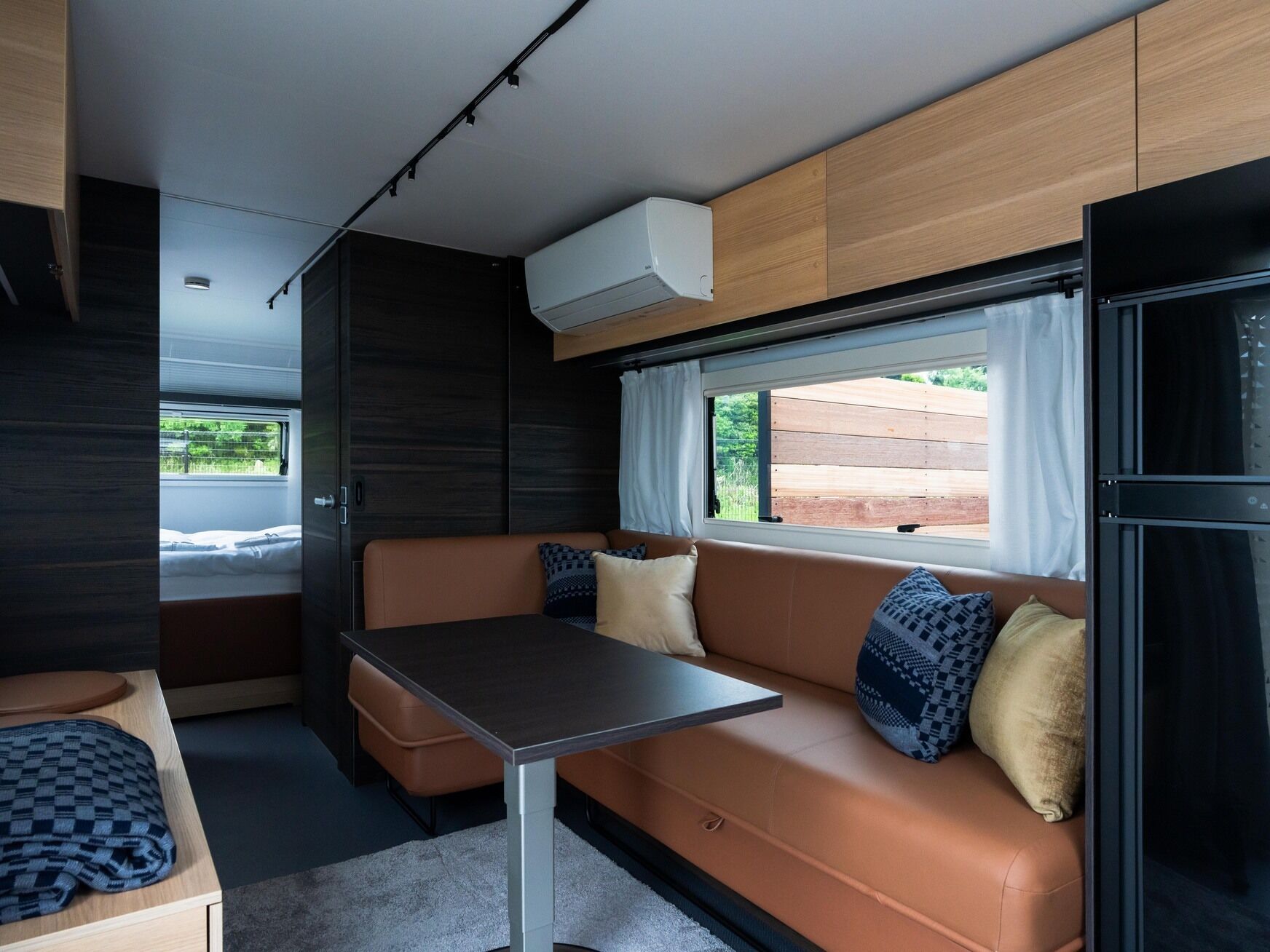 A compact RV interior with a sofa, table, and a window providing a view of the outdoors.