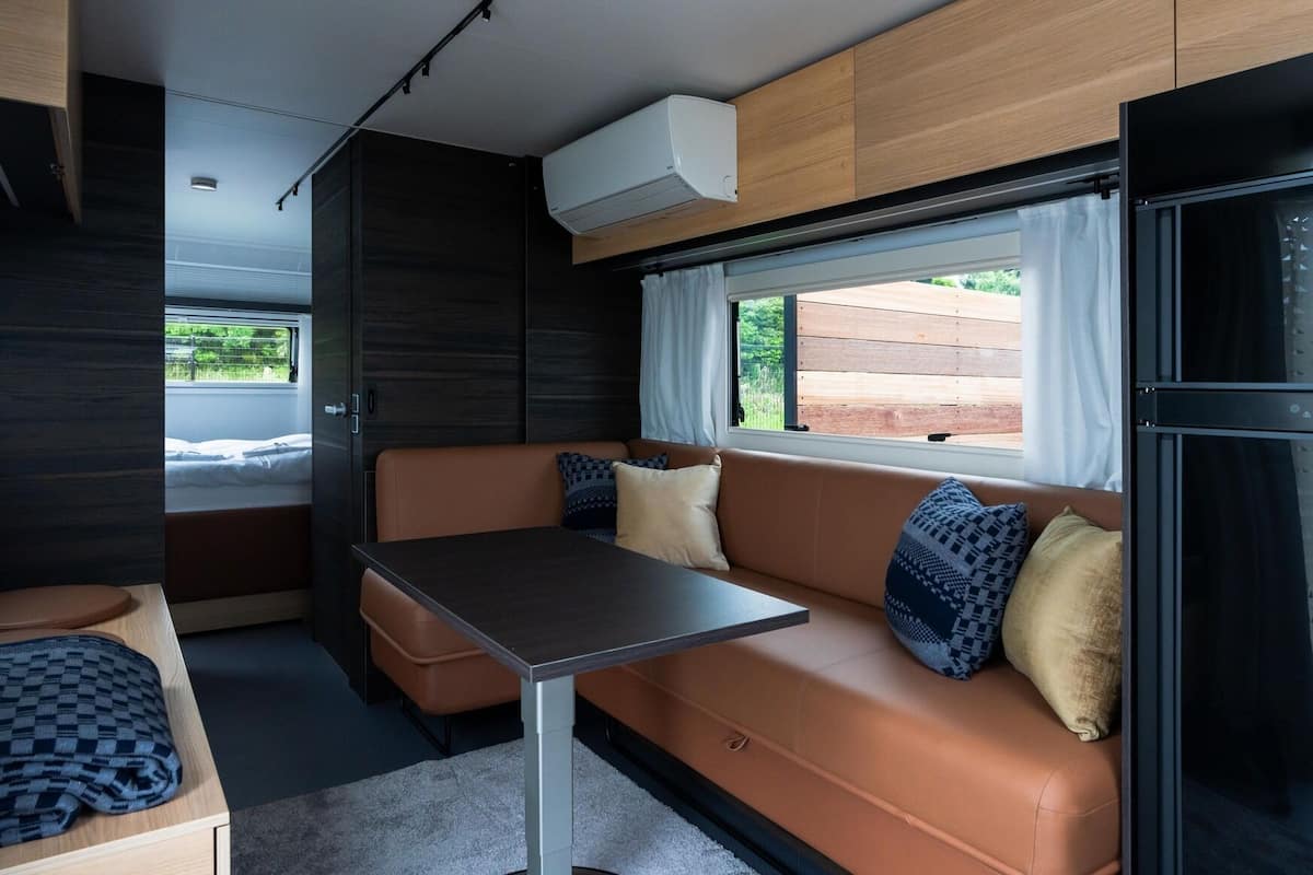 A compact RV interior with a sofa, table, and a window providing a view of the outdoors.