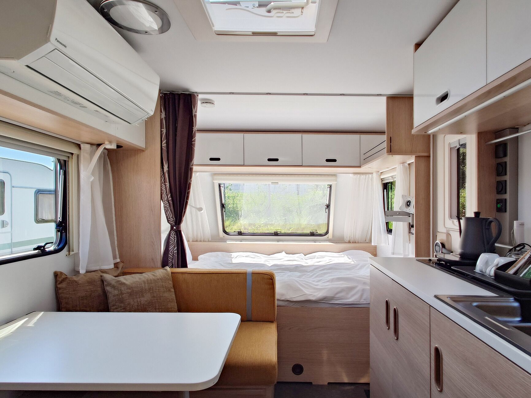 A compact RV interior with a bed, kitchenette, and a small dining area.