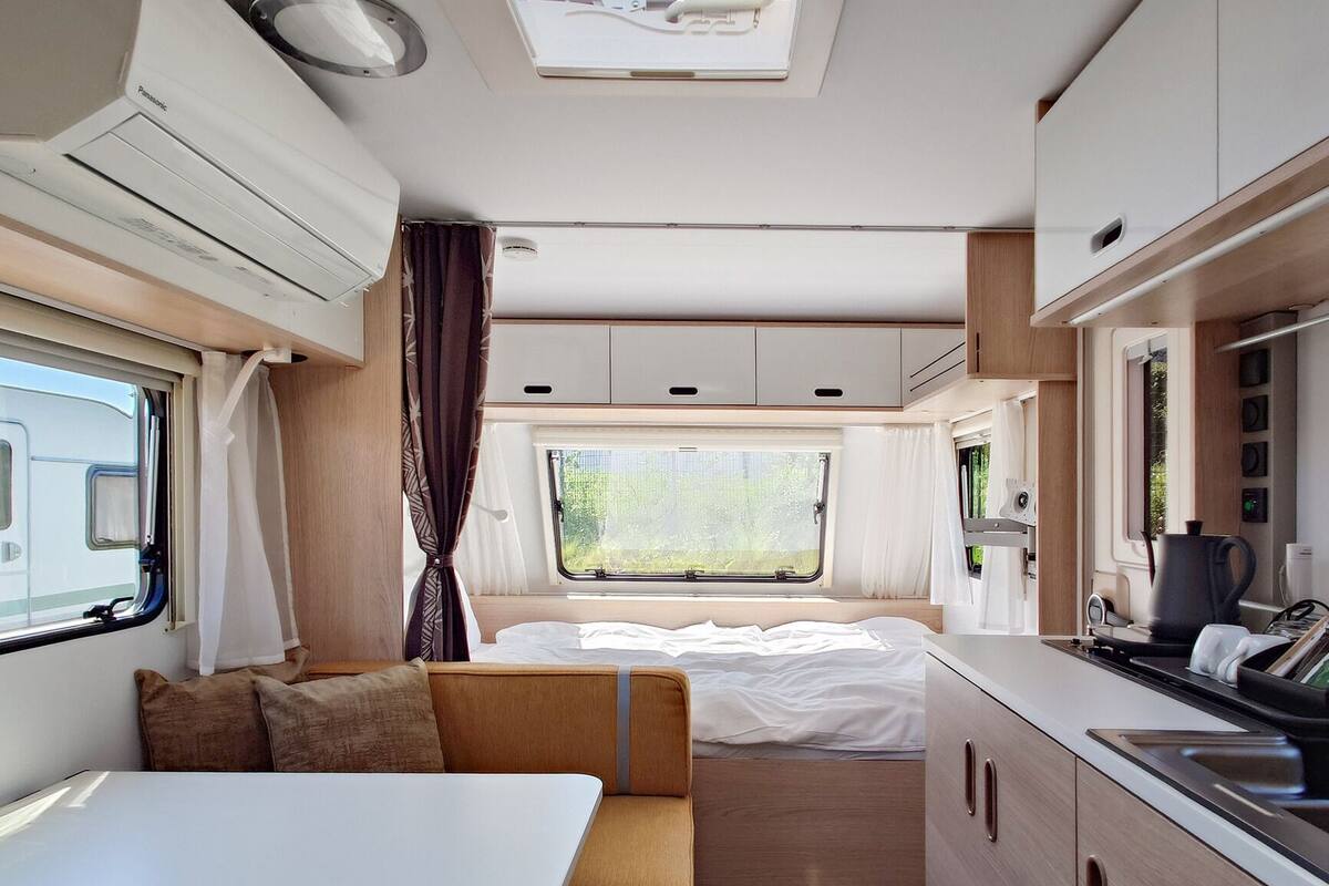 A compact RV interior with a bed, kitchenette, and a small dining area.