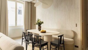 Un comedor moderno con una mesa redonda, cuatro sillas, un jarrón con flores y un sofá color beige.