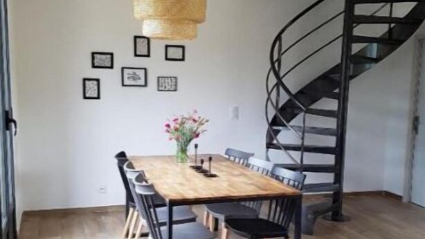 Un comedor con una mesa y sillas de madera, una lámpara colgante, cuadros en la pared y una escalera de caracol.