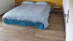 Un dormitorio con cama, piso de madera, una pared de acento amarilla y dos espejos adosados.