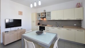 Et moderne køkken med et fladskærms-tv, spisebord med stole og et indbygget ovn.