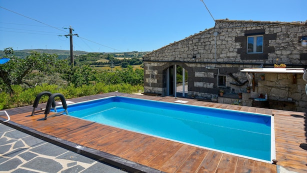 A swimming pool with a wooden deck, a stone building with a window, and a view of hills in the background. - Stunning home in Monterosso Almo (Monterosso Almo)