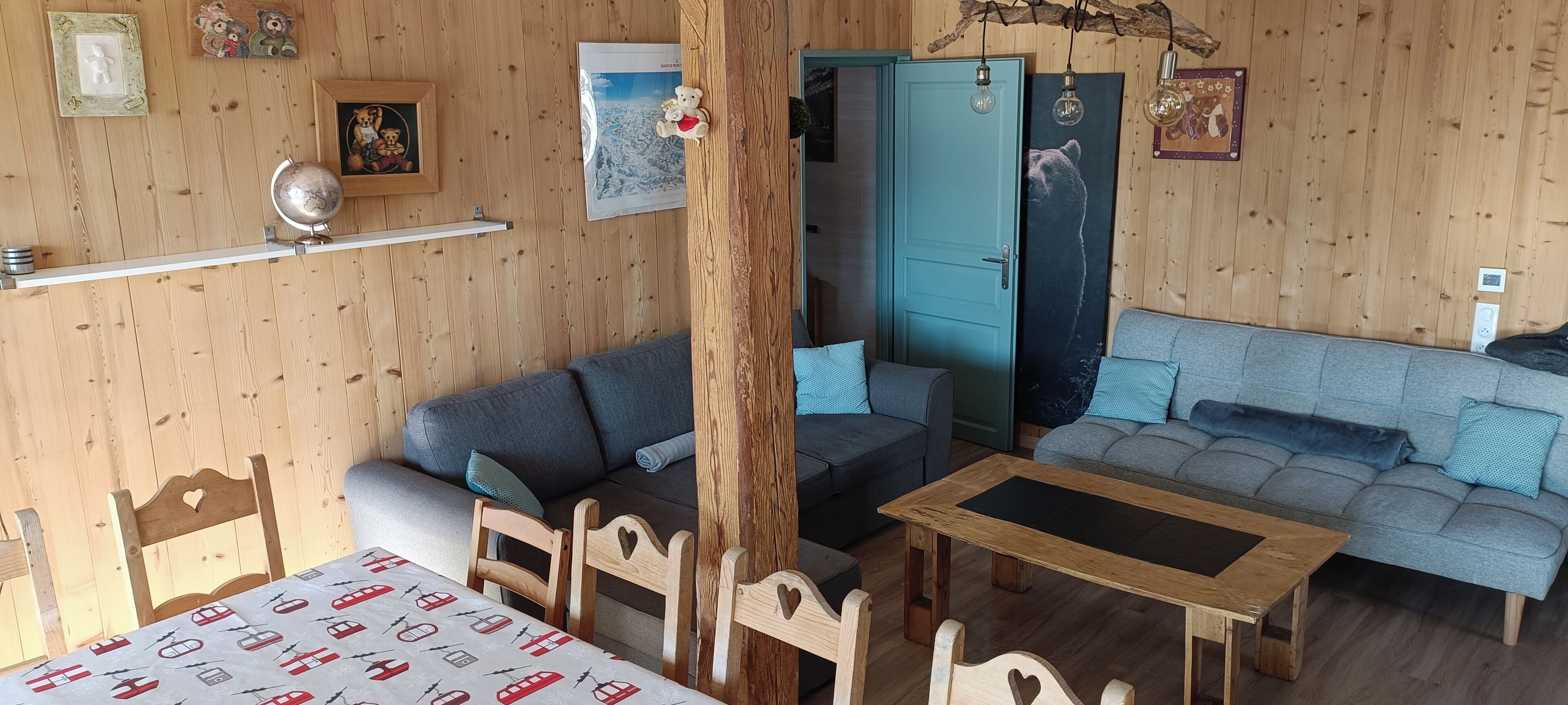 Een gezellige kamer met een houten inrichting, een blauwe deur, een grijze bank, een houten tafel en een wereldbol op een plank.