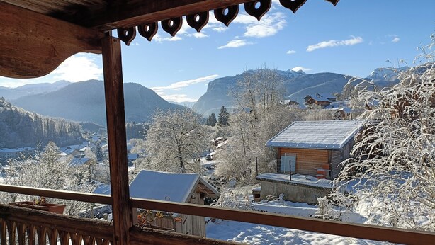 Un balcón de madera con vistas a un paisaje montañoso cubierto de nieve, que incluye casas y árboles.