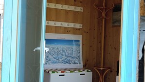 Un interior de madera con una puerta de cristal, un perchero, una mesita y un cuadro en la pared.