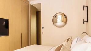 A hotel room with a bed, a TV mounted on the wall, a round mirror, and a wardrobe.
