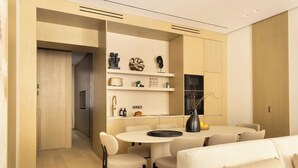 A modern living room with a sofa, a dining table with chairs, and a kitchen area with shelves and a TV.