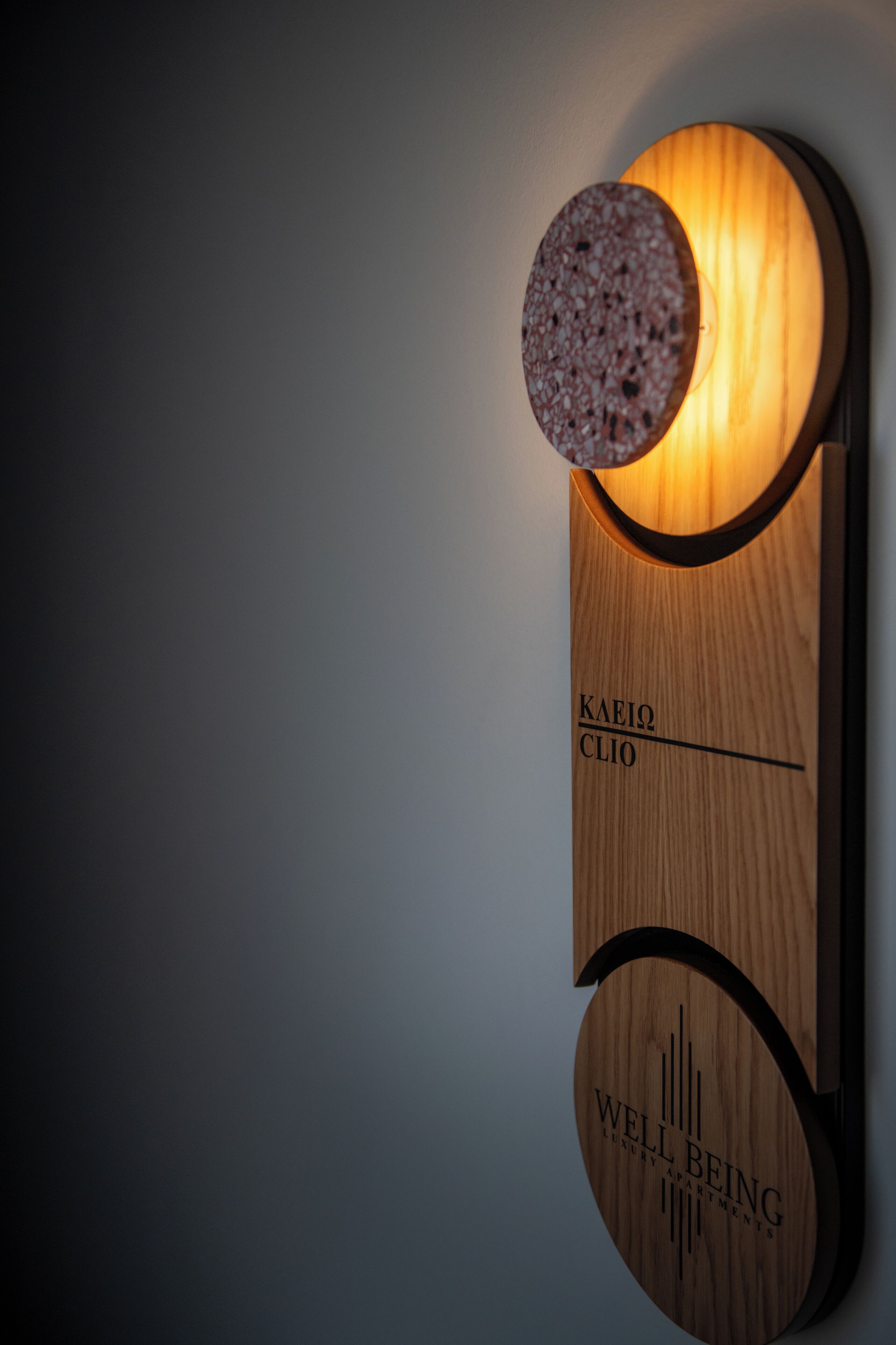 A wooden wall-mounted sign with the text "KAEIJ CLIO" and "WELL BEING LUXURY APARTMENTS".