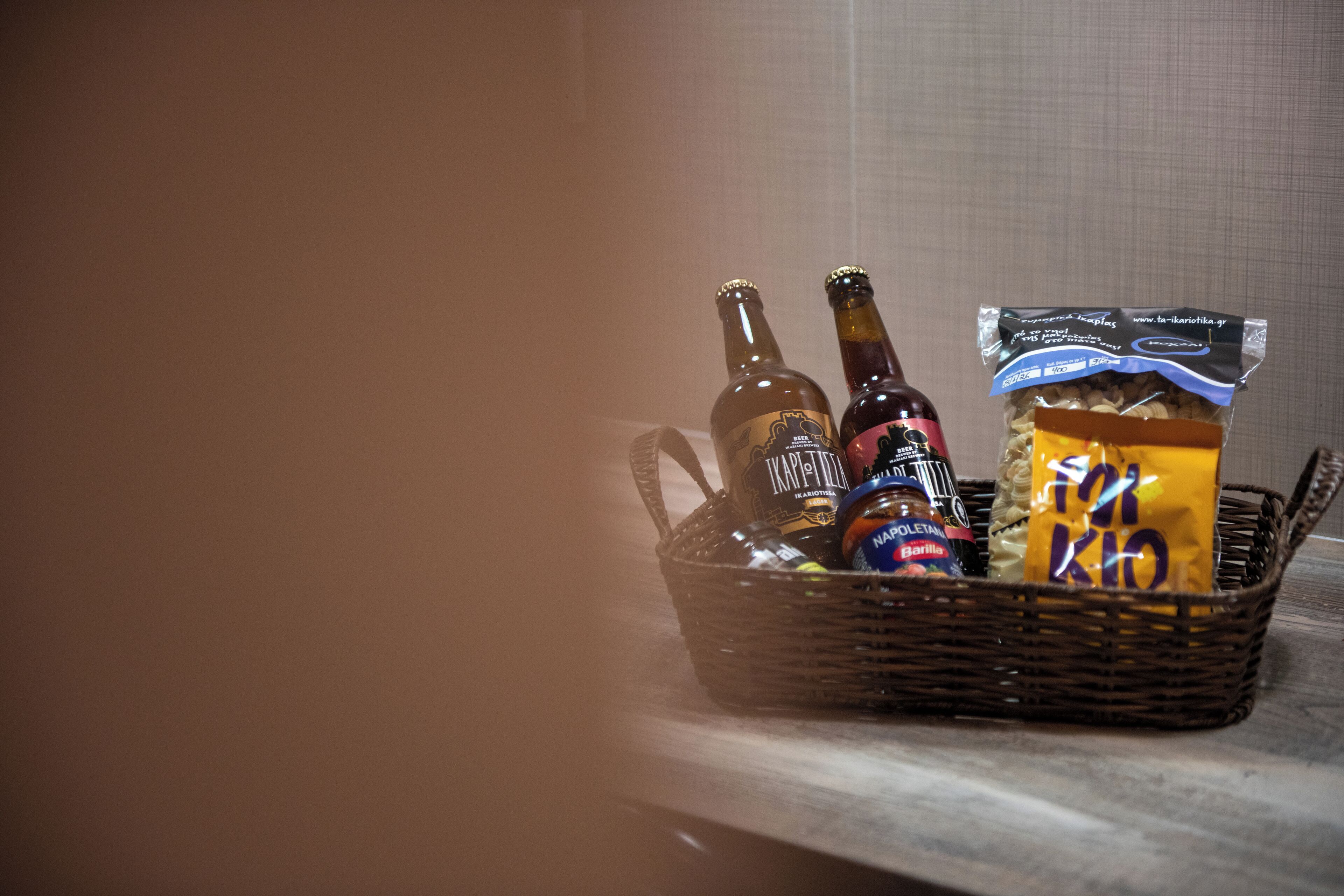 Un panier en osier contenant deux bouteilles de bière, un pot de sauce et un paquet de collations.