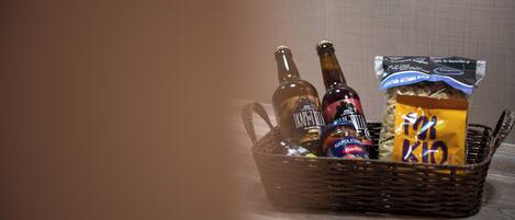 A wicker basket containing two bottles of beer, a jar of sauce, and a packet of snacks.