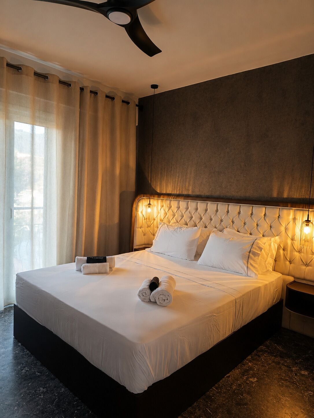 A hotel room with a large bed, a ceiling fan, and a view of the outdoors.