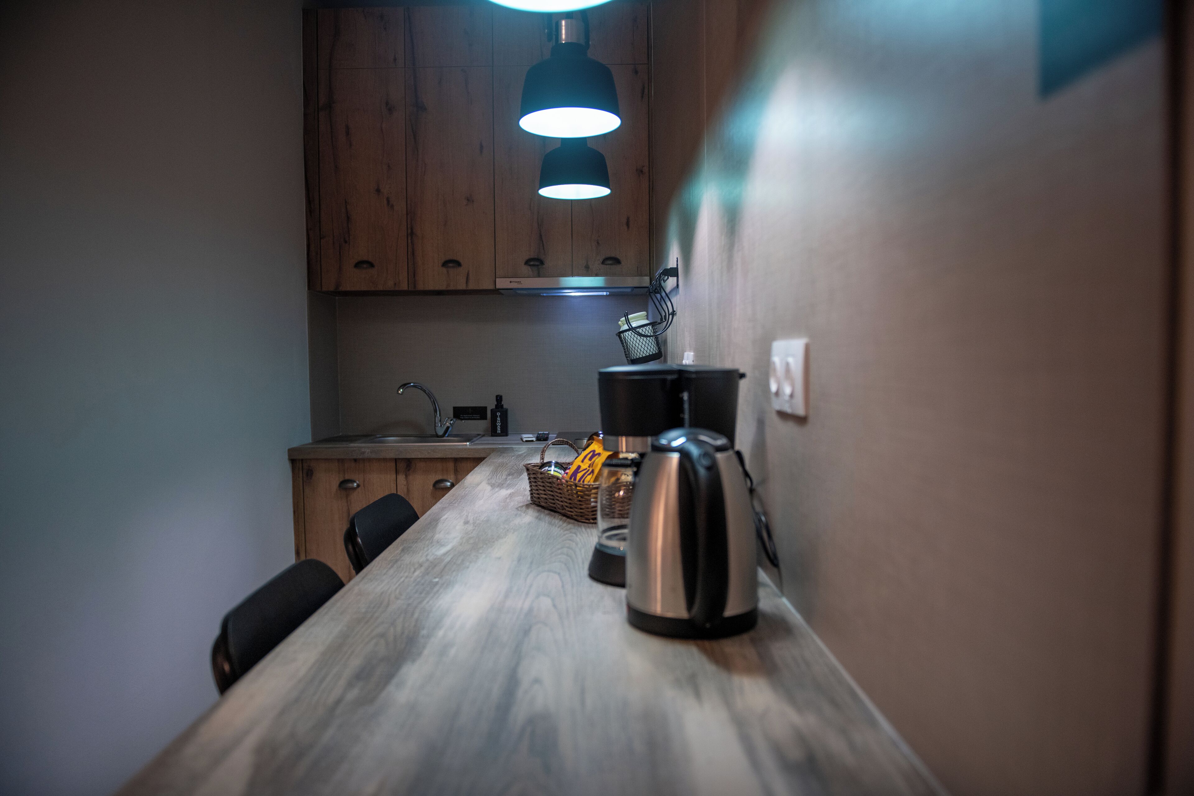 Una cocina con armarios de madera, una tetera de acero inoxidable, una cafetera y una cesta con aperitivos.