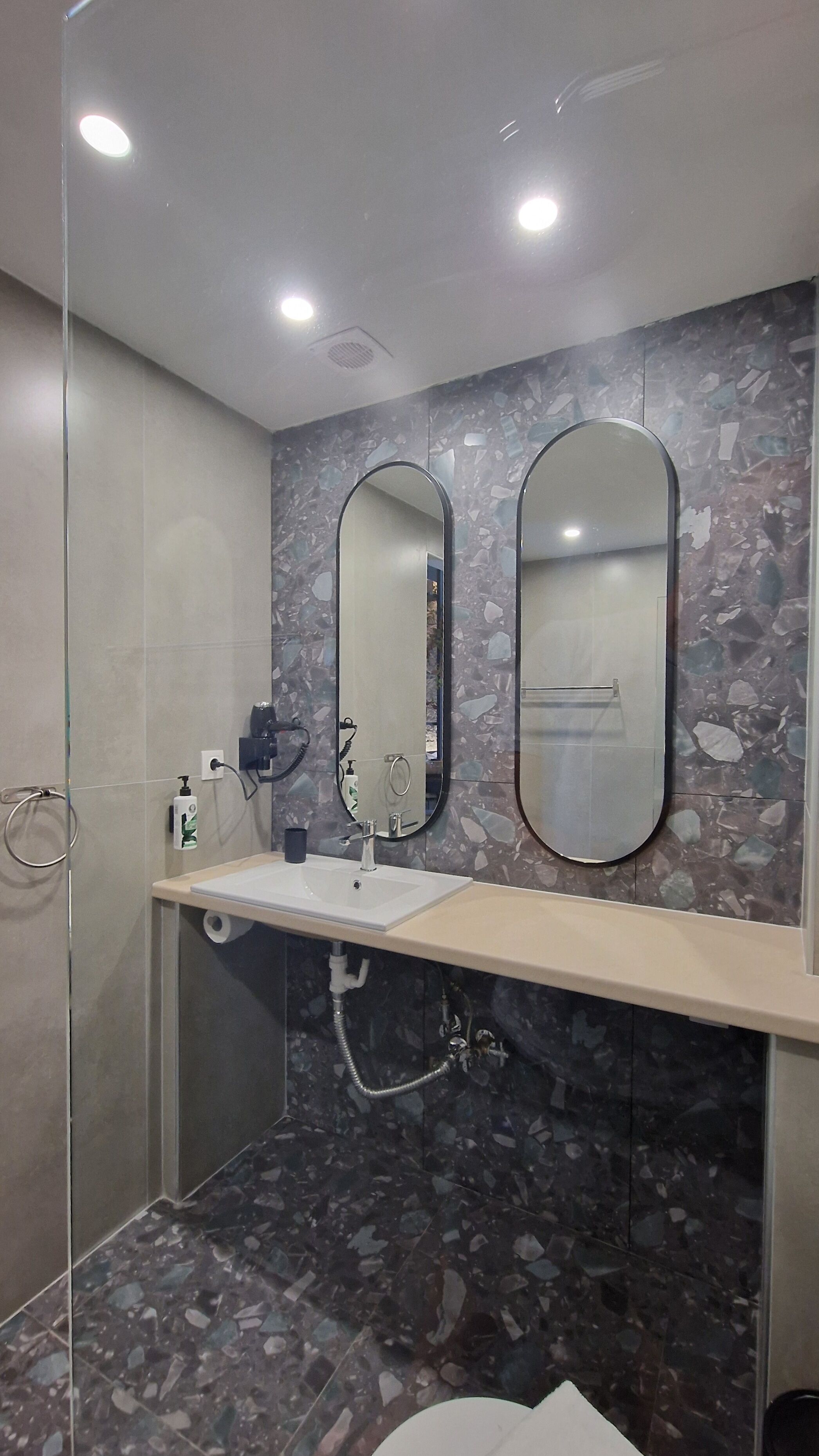 A bathroom with a glass shower enclosure, a sink with a mirror above, and a marble backsplash.