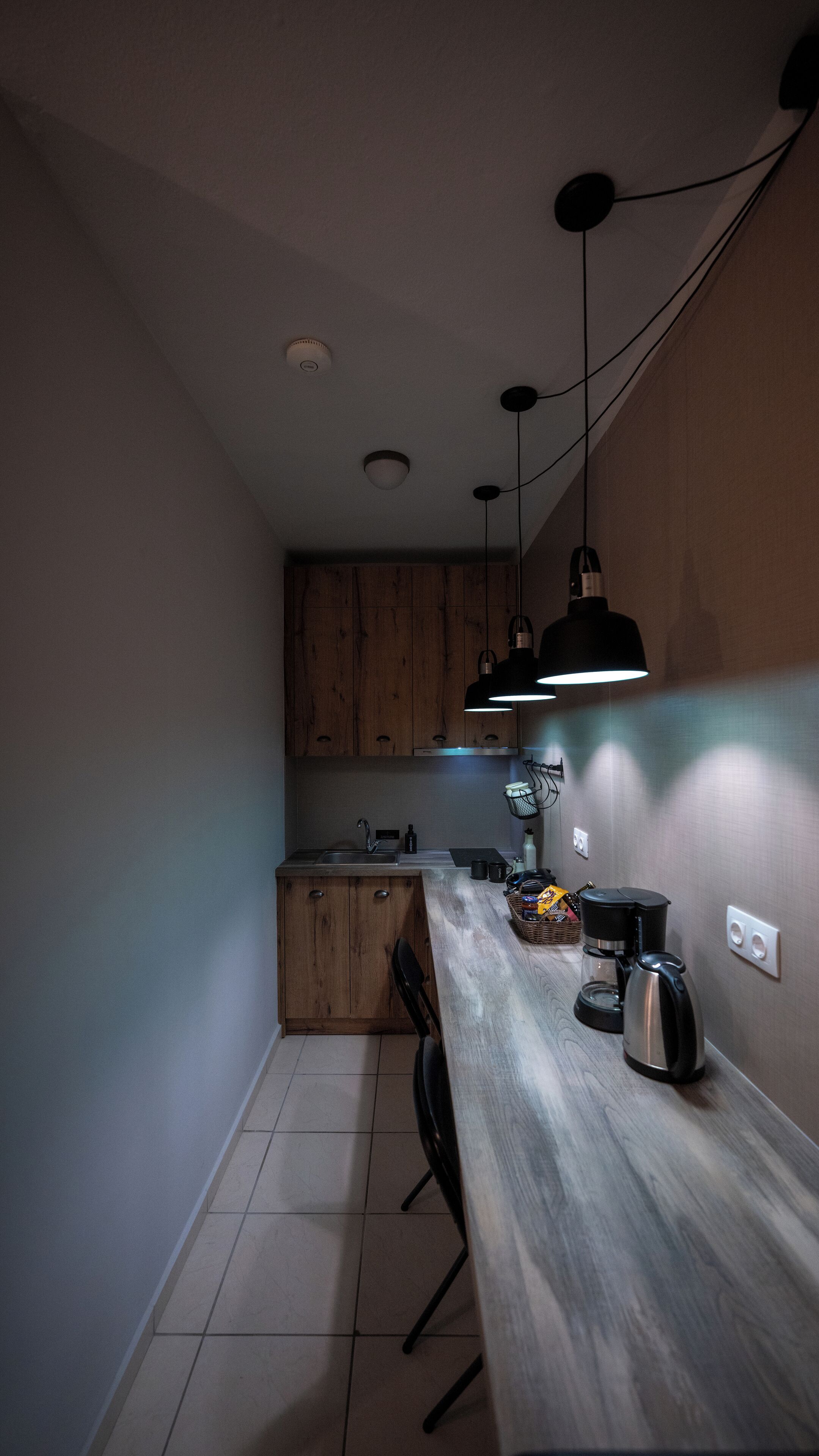 A narrow kitchen with wooden cabinets, a long countertop, and a coffee maker.