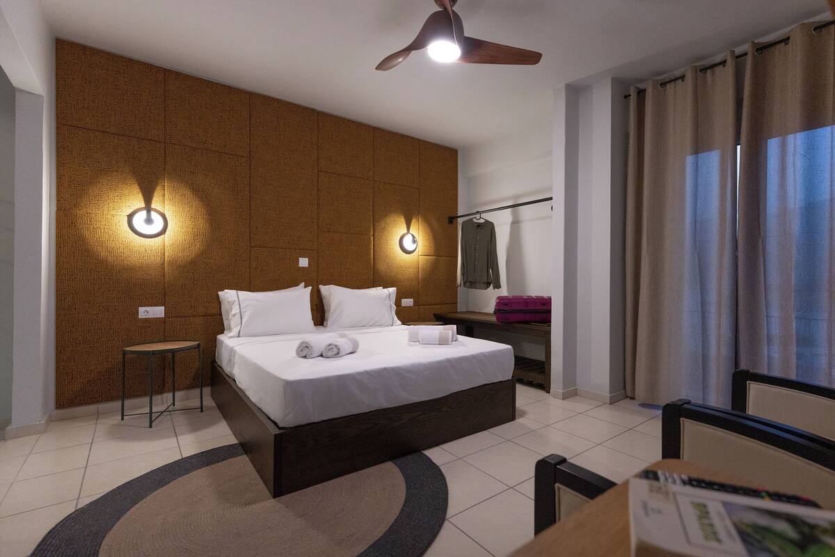 A modern hotel room with a large bed, two bedside lamps, a ceiling fan, a small table, and a chair.