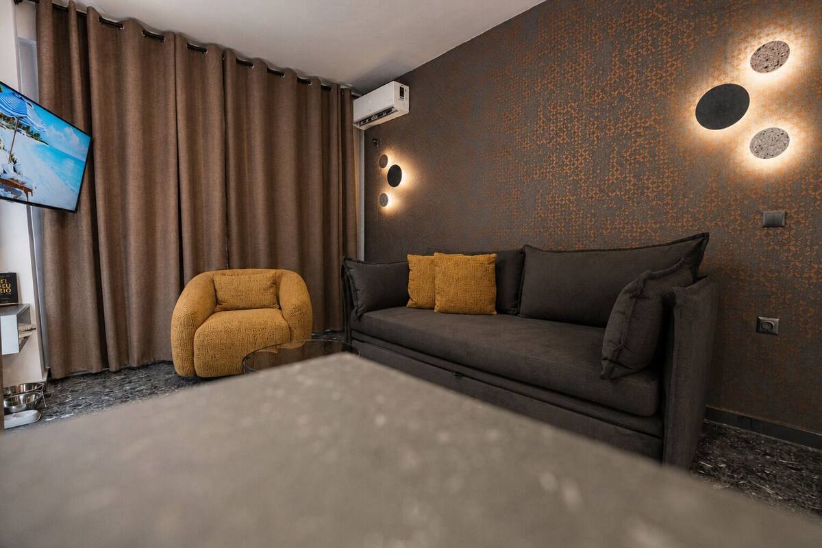 A modern living room with a sofa, a round armchair, a flat-screen TV, and a wall-mounted air conditioner.