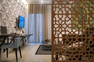 A modern hotel room with a desk, chair, and a TV. There is a window with curtains and a decorative screen.