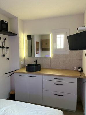 A modern kitchen with a round black sink, a mirror with integrated lighting, a flat-screen TV mounted on the wall, and a window with a view of the outside. - St Cyprien Ground floor apartment with large terrace overlooking the Marina! (Saint-Cyprien)