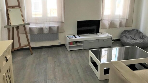 Una sala de estar moderna con televisor, sofá, sillón de peluche, mesa de centro de vidrio y una mesita con un cuadro.