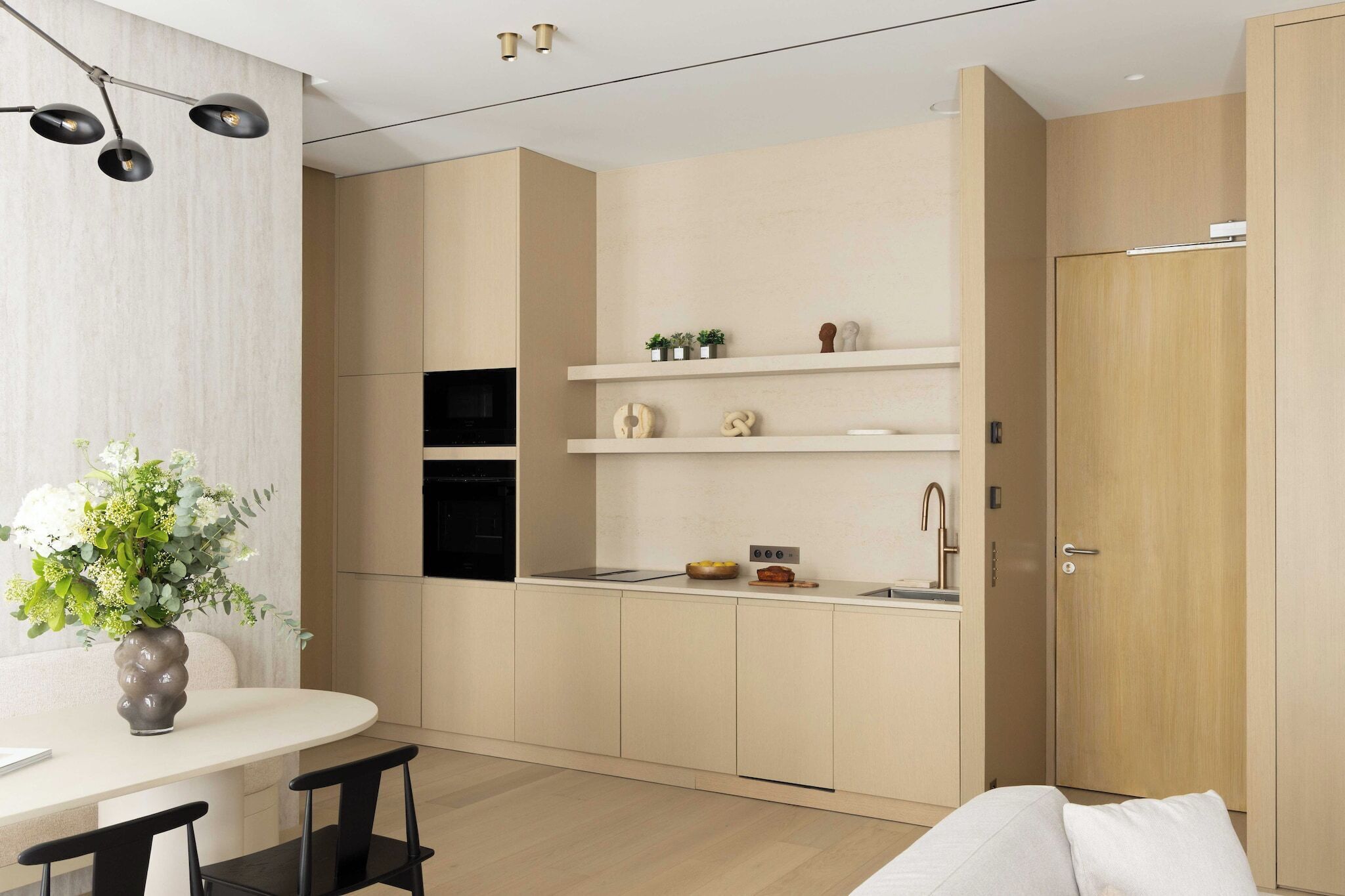 A modern kitchen with built-in appliances, a dining area with a white table and black chairs, and a wooden wardrobe.