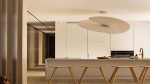 A modern kitchen with white cabinets, a central island with stools, and a unique pendant light.