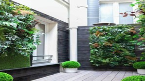 A modern outdoor space with a wooden deck, a vertical garden, and a small seating area.