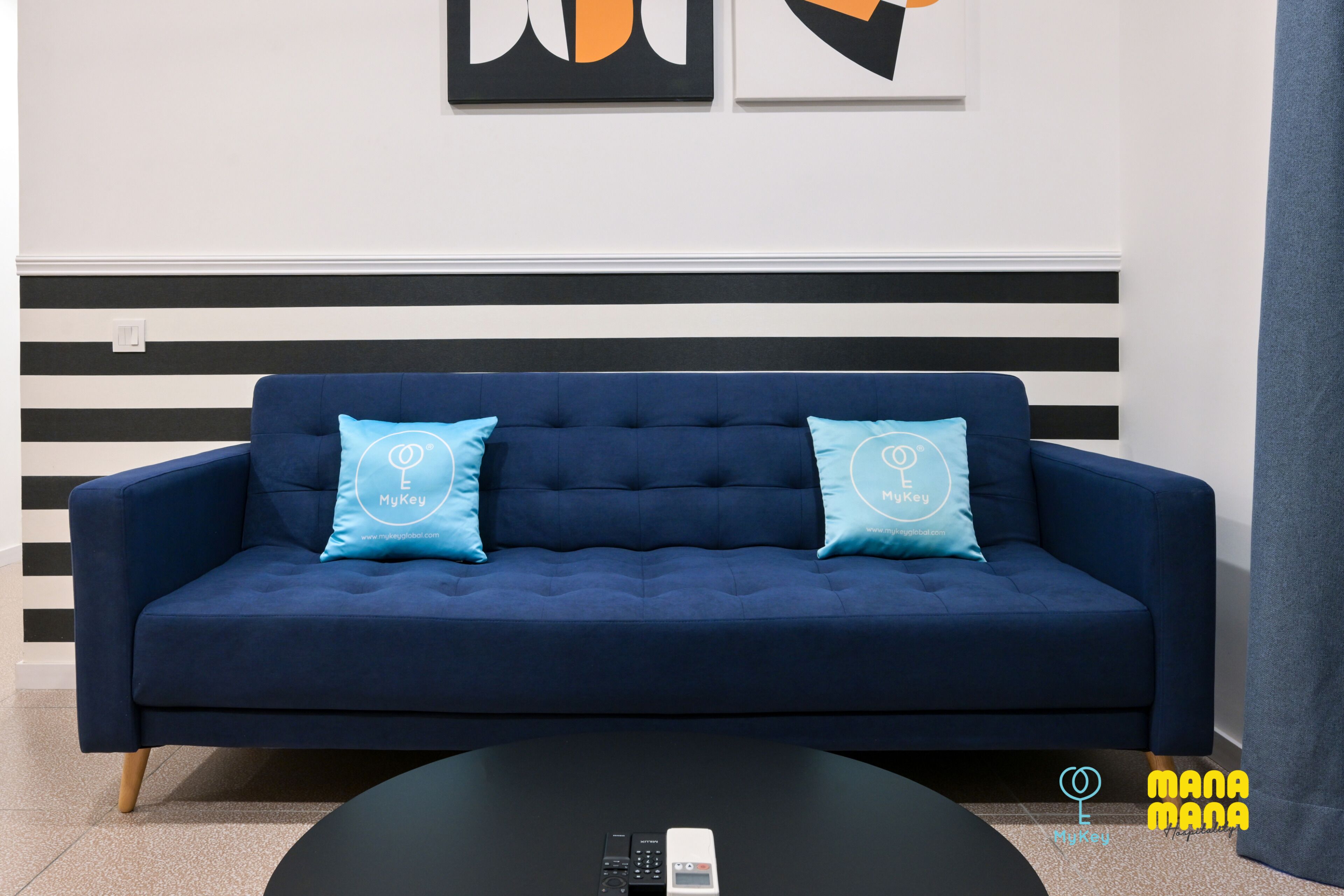 Un salon moderne avec un canapé bleu foncé, deux coussins bleu clair et une table basse noire avec une télécommande.