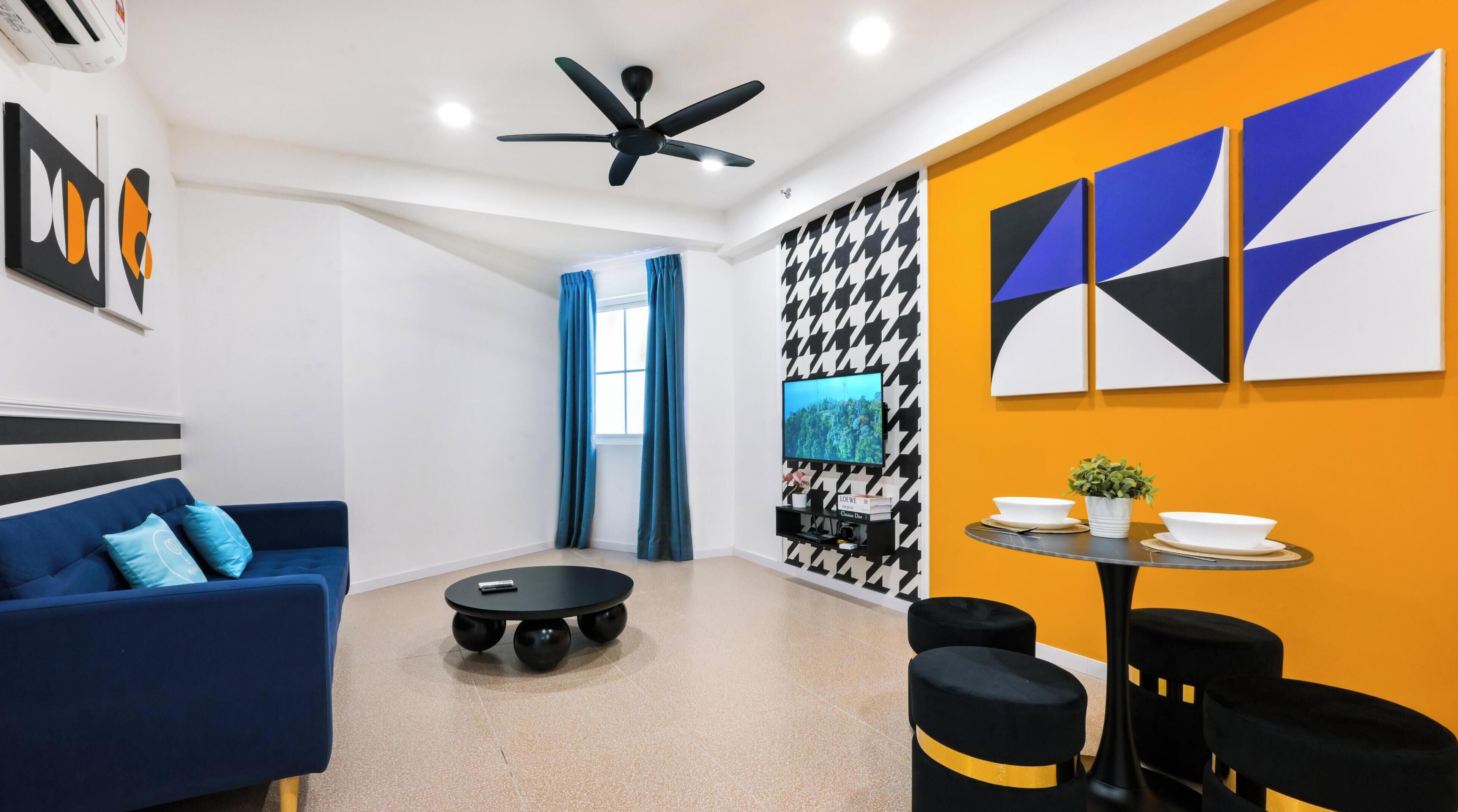 Een moderne woonkamer met een blauwe bank, een ronde salontafel, een plafondventilator en een televisie bevestigd aan een muur met een hondentandpatroon.