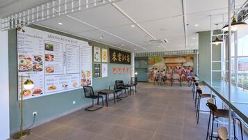A spacious restaurant interior with a high ceiling, a menu board on the left, and a seating area with tables and chairs.