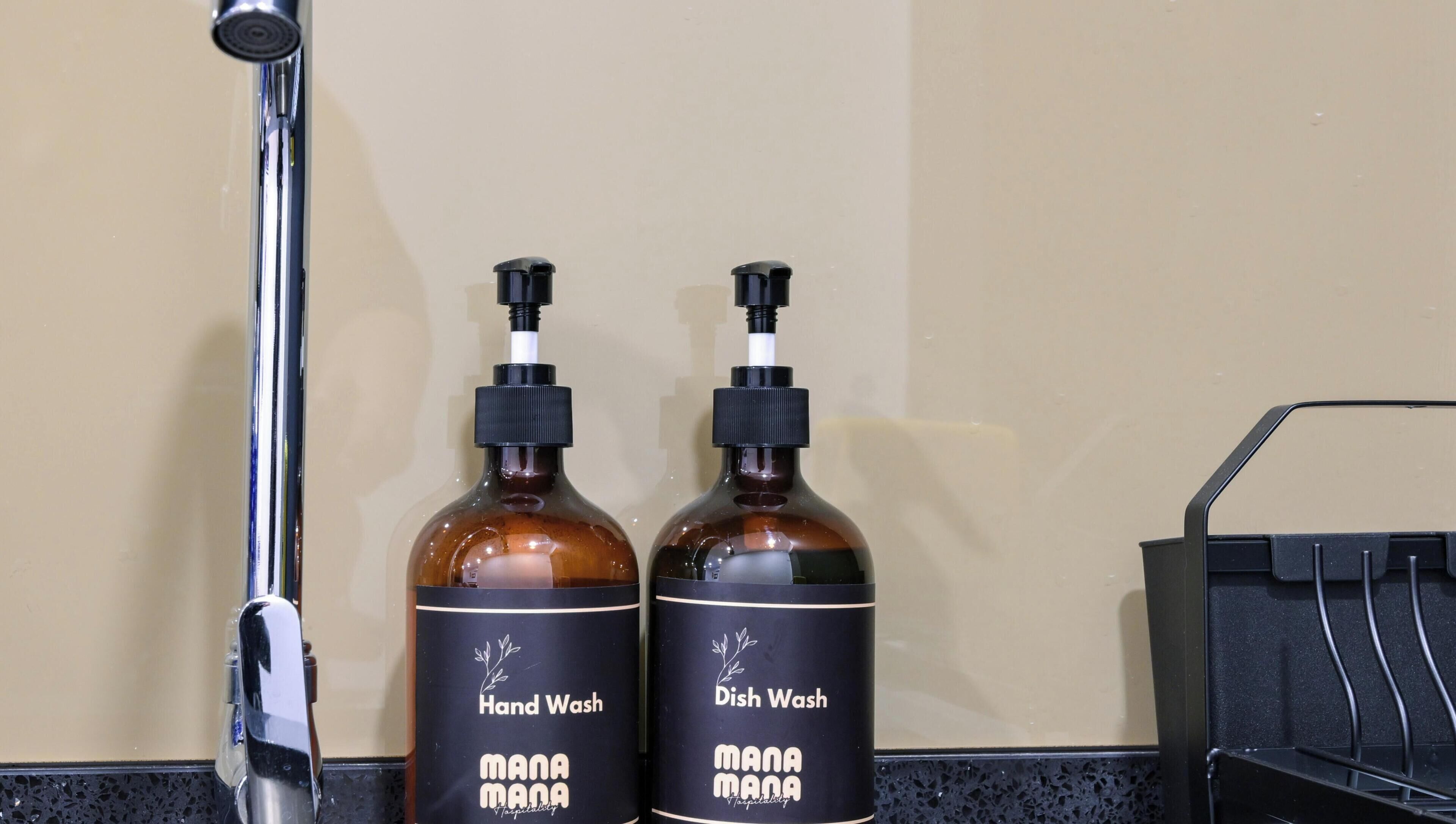 Two bottles of hand and dish soap labeled 'MANAMANA' on a counter next to a faucet.