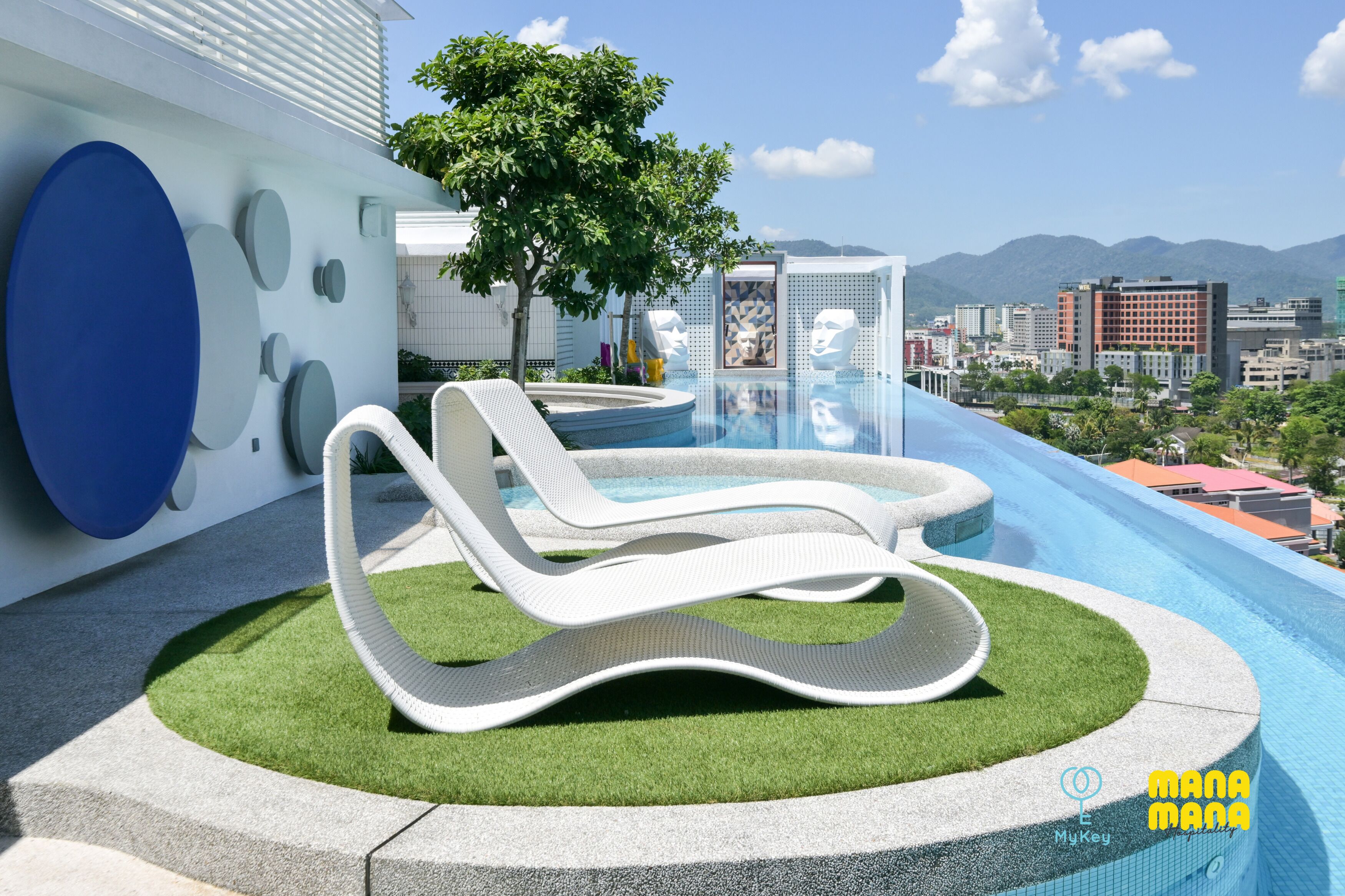 Zona de piscina moderna a l'aire lliure amb gandules, un arbre i vistes a la ciutat.