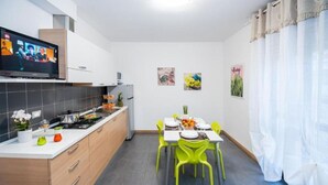 Moderni keittiö, jossa on ruokailutila, televisio, puukalusteet ja ruokapöytä neljälle henkilölle.