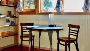 Ett rum med ett runt bord, två stolar, en lampa, en bokhylla och ett fönster med gardiner.