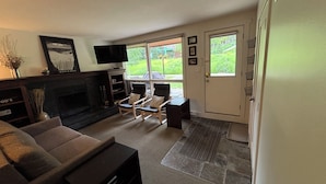 A living room with a fireplace, a sofa, a television, and a door leading to a garden. - Slope Side Studio Panorama Resort (Panorama)