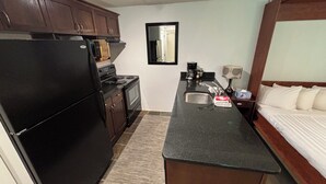 A compact kitchen with a refrigerator, stove, and microwave. There's a sink with a towel and a tissue box. A bed with white bedding is visible. - Slope Side Studio Panorama Resort (Panorama)