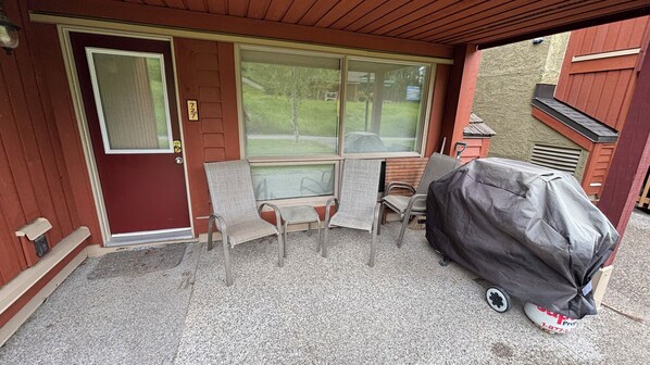 A covered patio with a grill, a sliding glass door, and a bench.