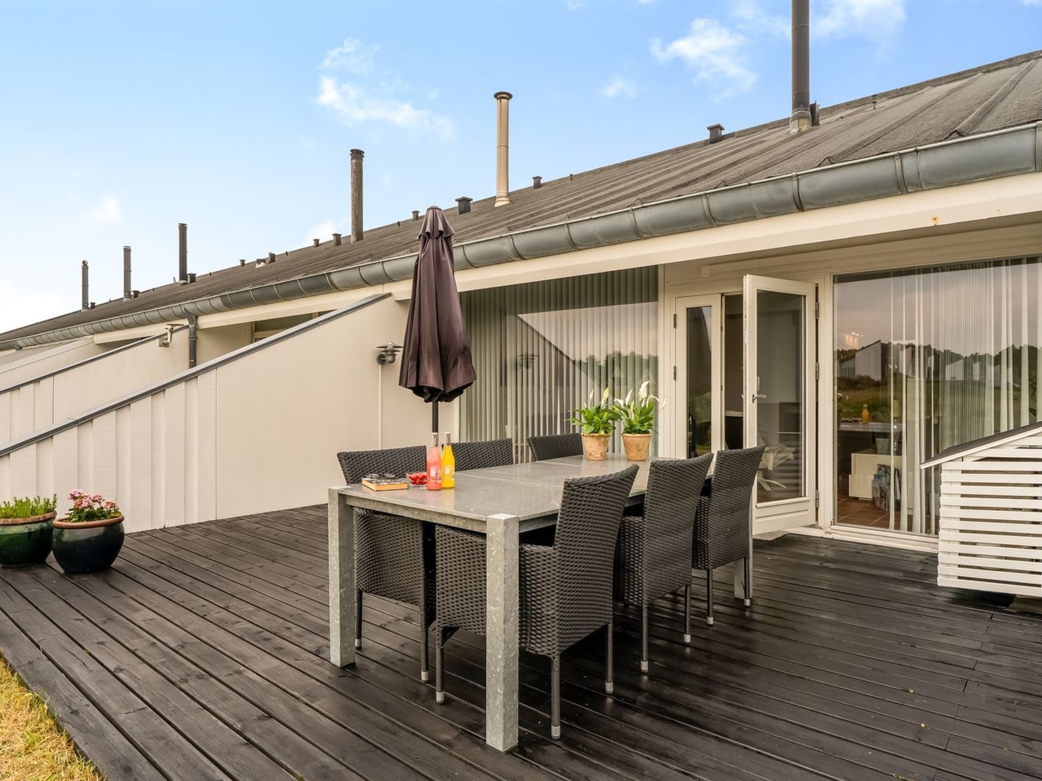 A covered outdoor patio with a table and chairs, potted plants, and a sliding glass door leading to a covered area.