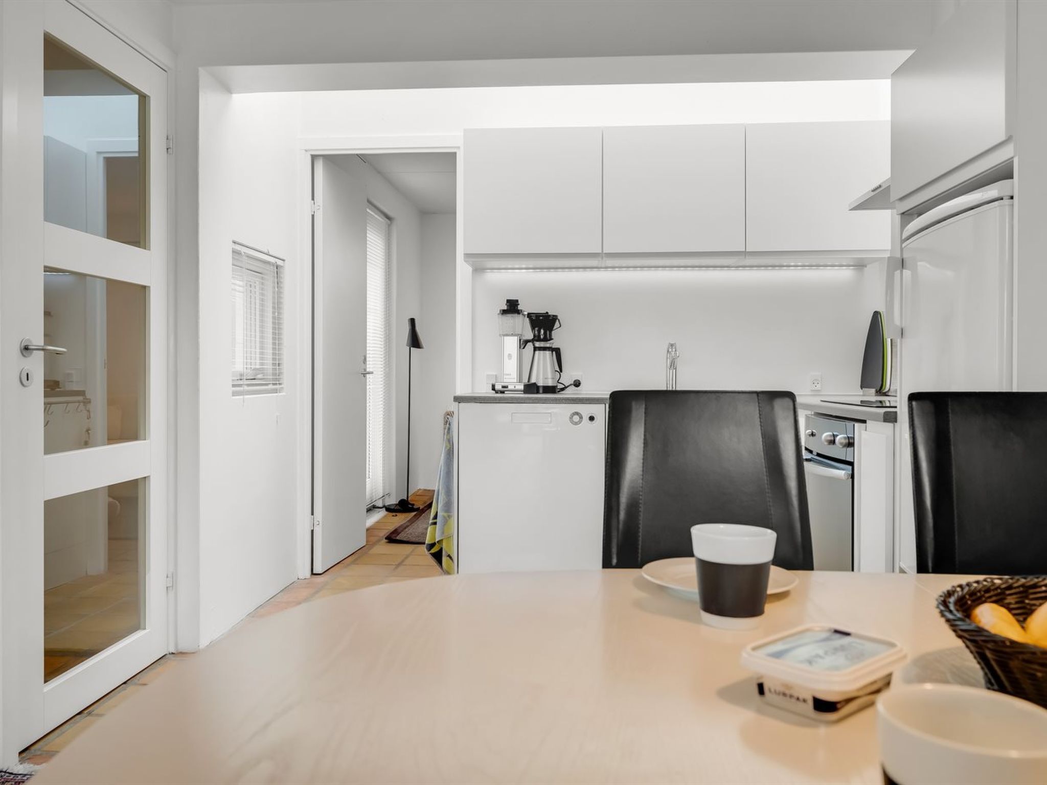 Ett modernt kök med vita skåp, en kaffemaskin och en matplats med ett bord och stolar.