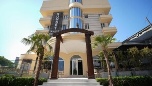 Un hôtel à plusieurs étages, doté d’une entrée imposante, de palmiers et surplombant un ciel dégagé.